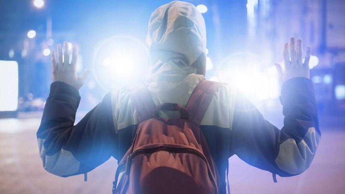 male suspect arrested in the night city, with police flashers behind him